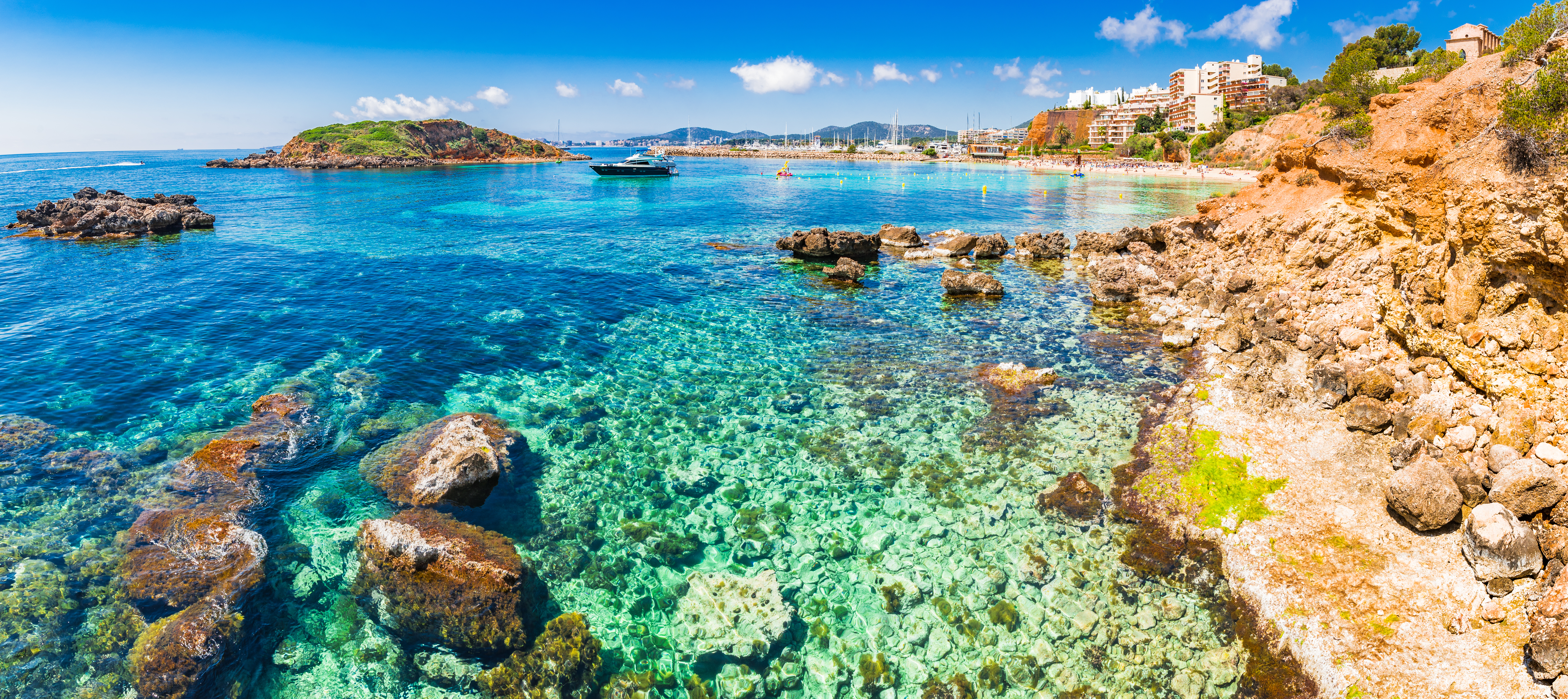 Kristallklares Wasser vor zerklüfteten Felsen in Cala Portal Nous