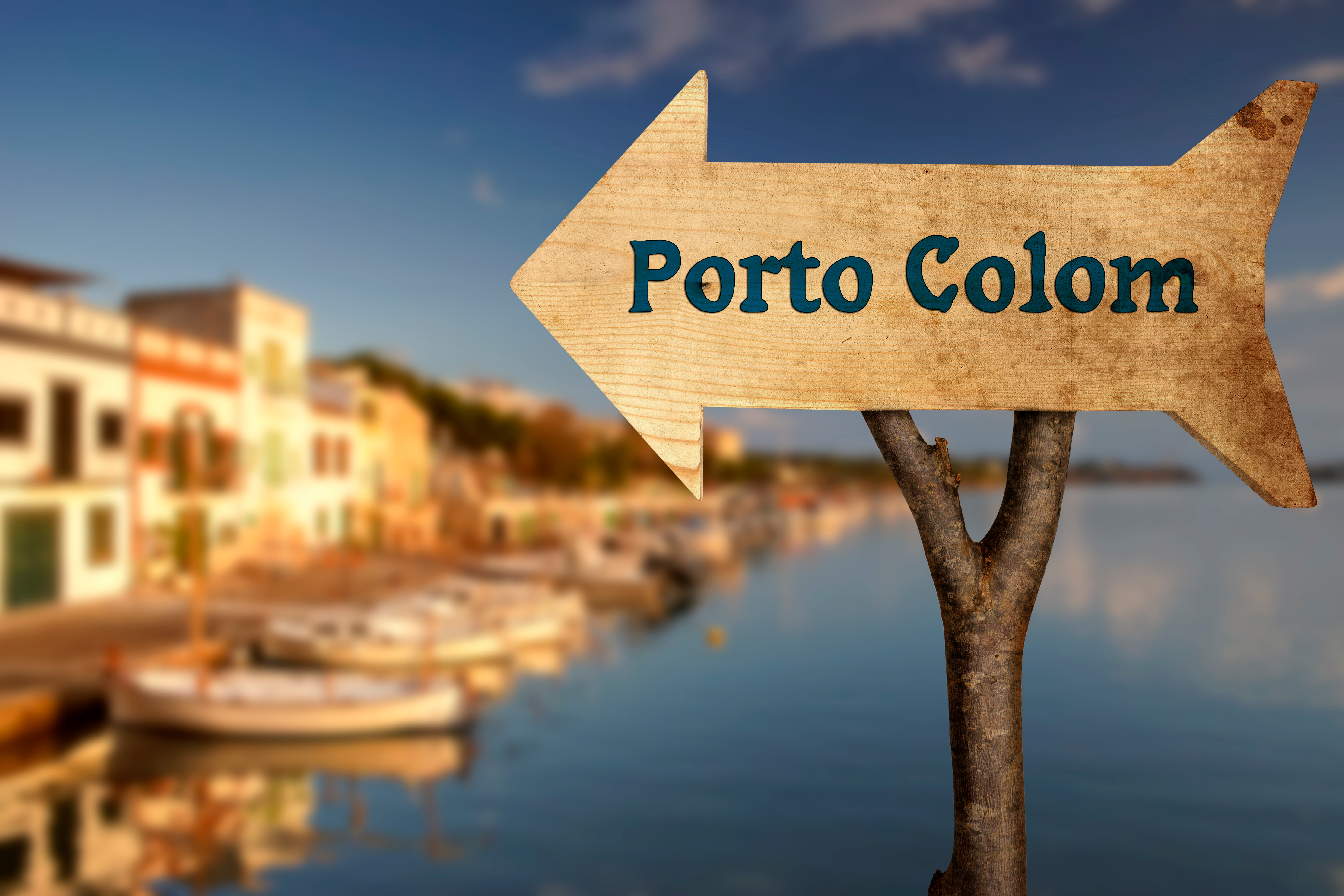 Signpost to Porto Colom. In the background the harbor with small fishing boats