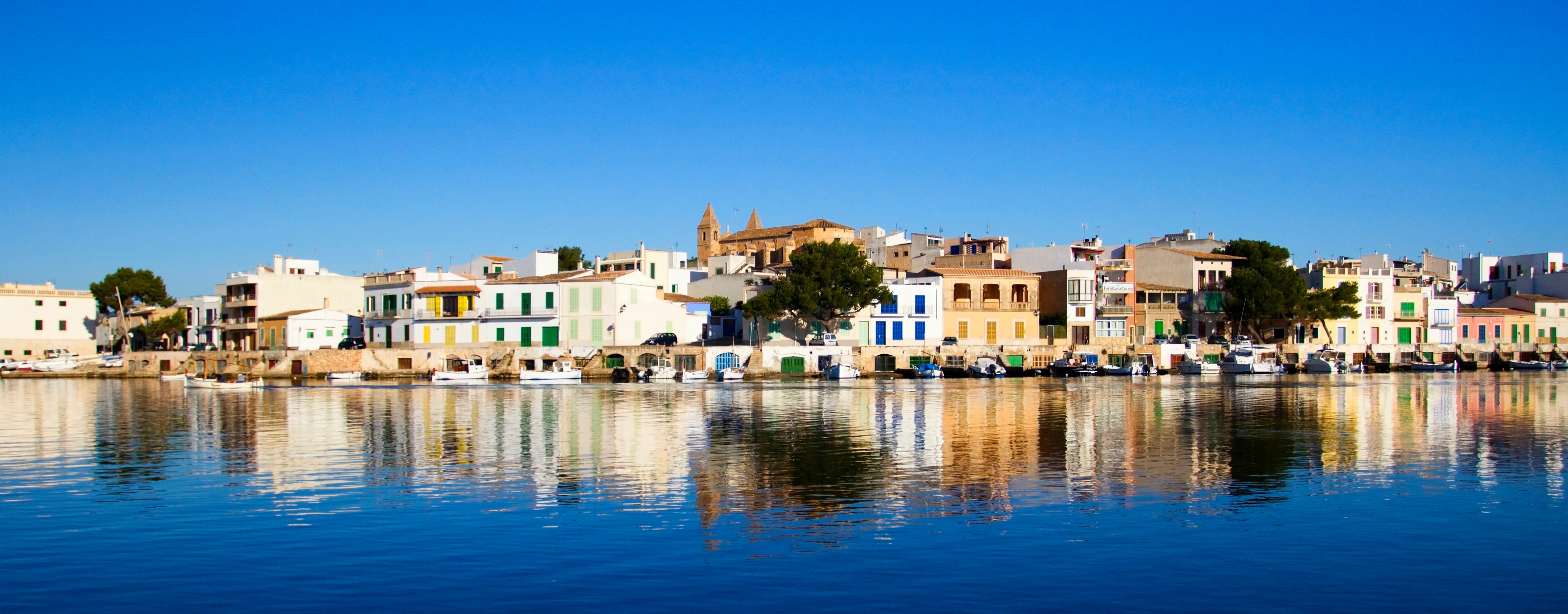 Küçük evler, parlak mavi gökyüzü ve Porto Colom koyunda sakin deniz