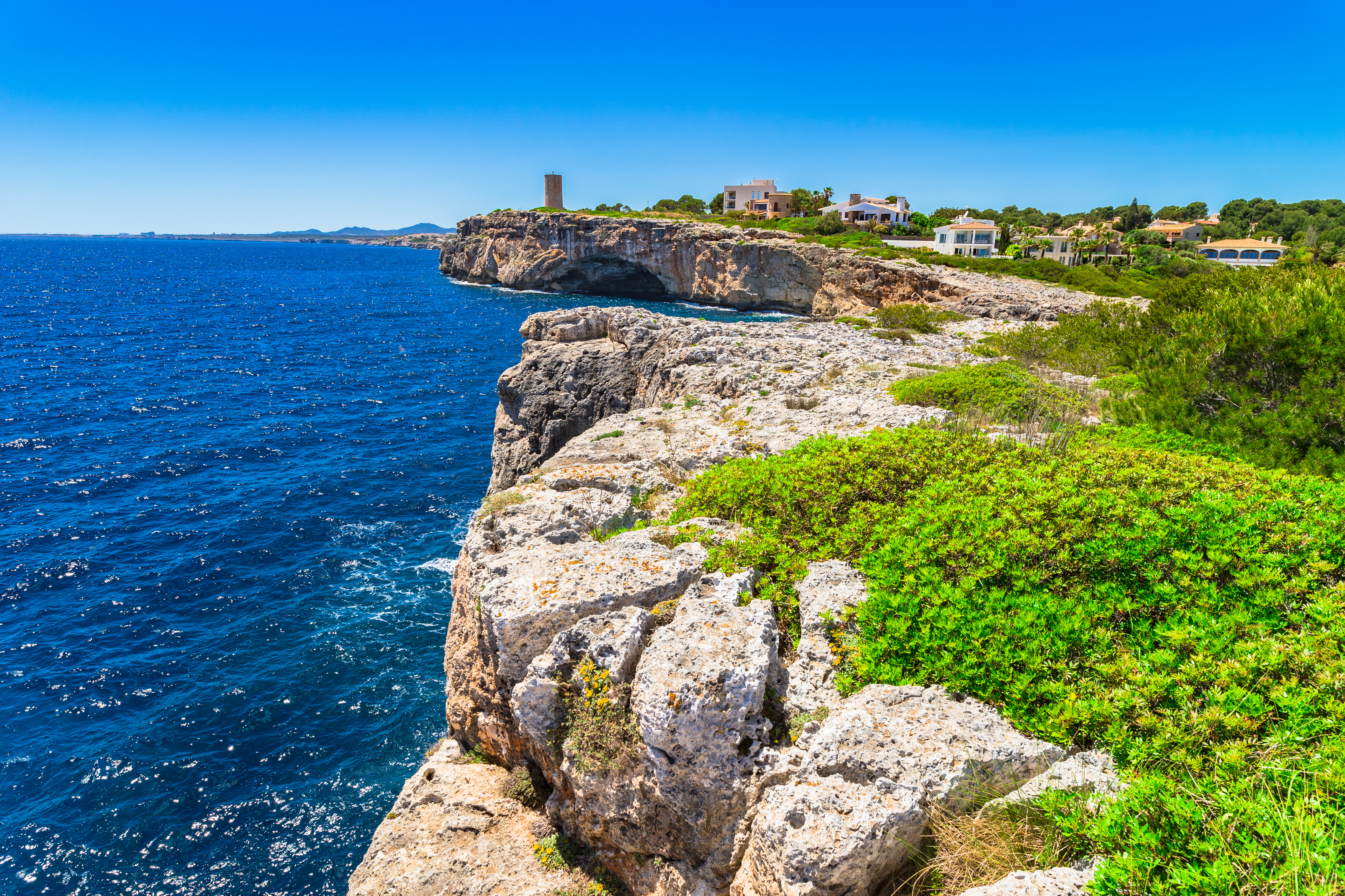 Porto Cristo'nun kayalık kıyısı, arka planda eski bir gözetleme kulesi