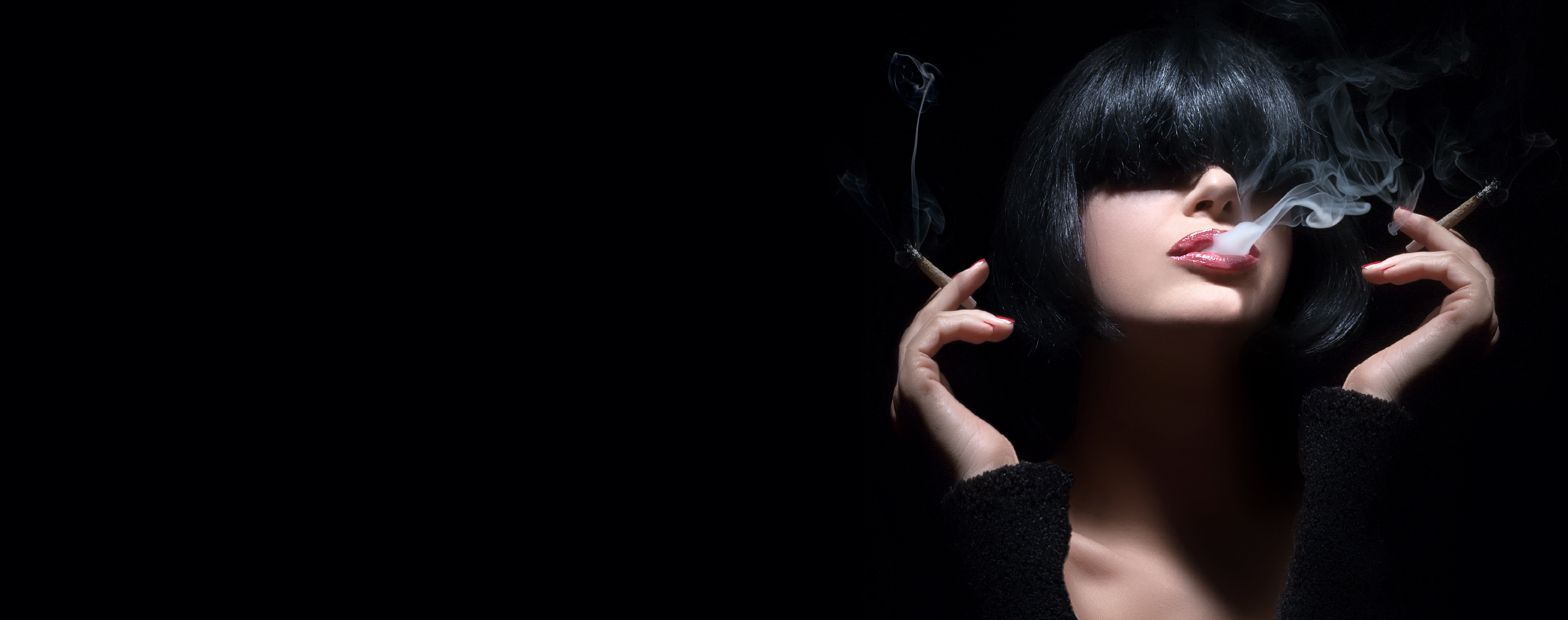 Attractive young woman smoking cannabis with two joints against a black background