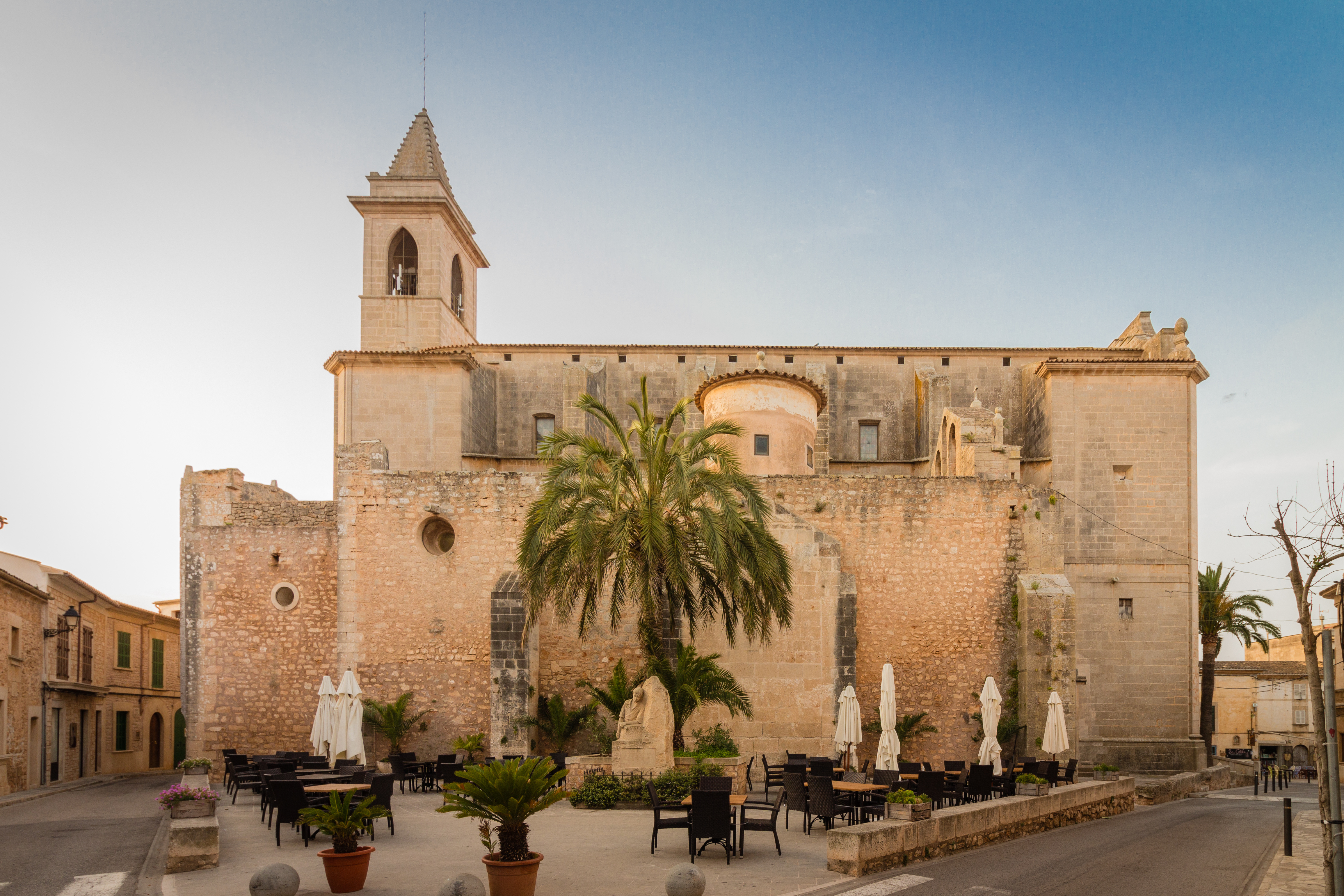 La vecchia chiesa di Santanyi al tramonto, con una palma imponente e tavoli e sedie che invitano a fermarsi