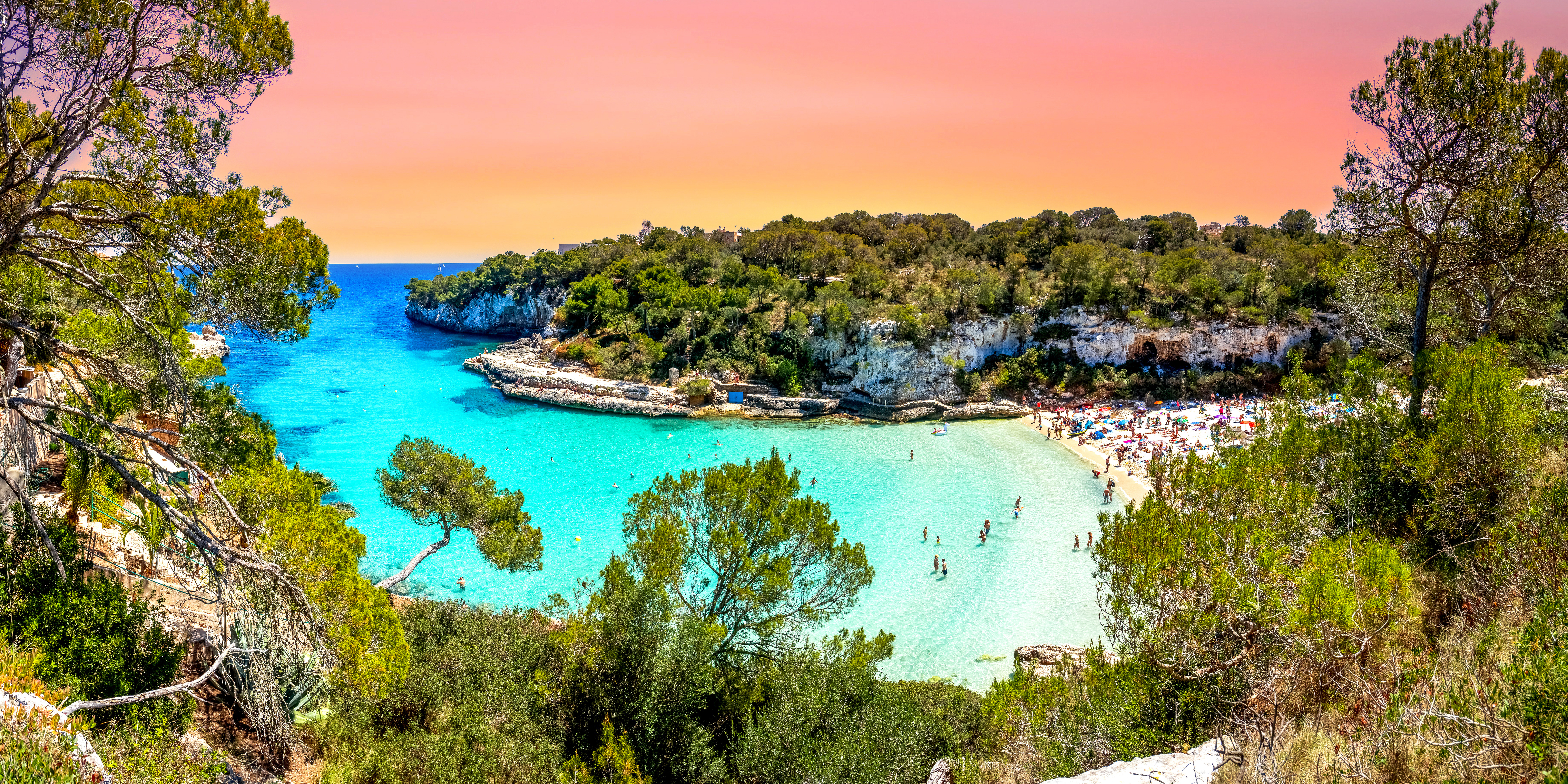 Vista sulla baia balneare con sabbia bianca come la neve di Cala Llombards. Acqua in varie tonalità di blu circondata da vecchi pini