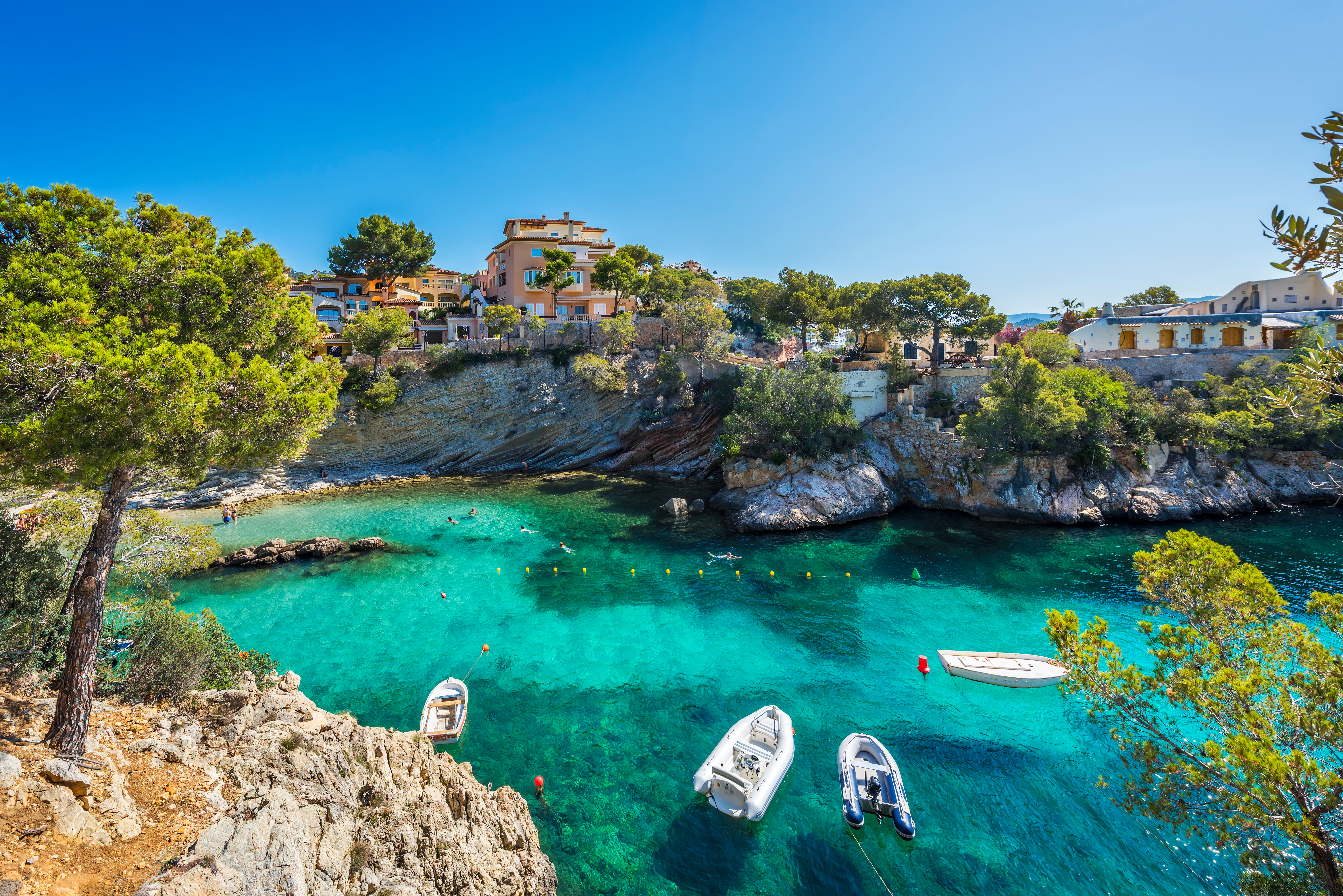 Kleine Fischerboote in der Bucht von Cala Fornells mit Felsküste und alten Häusern